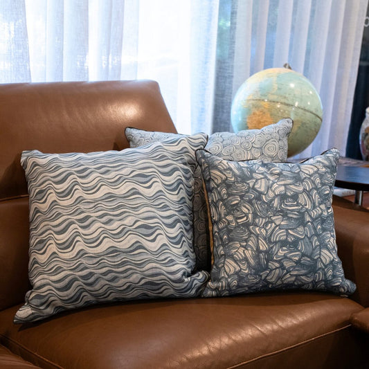 Three linen cushion covers styled on a brown leather chair, featuring the Frenchmans Pipi design alongside matching Starfish Studio patterns.