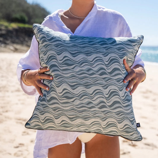 Frenchmans Straddie Stripe linen cushion cover held on the beach, showing the blue wave pattern.