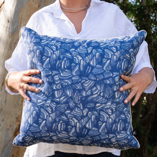 Woman holding square Pacific Pipi linen cushion cover in blue and natural tones