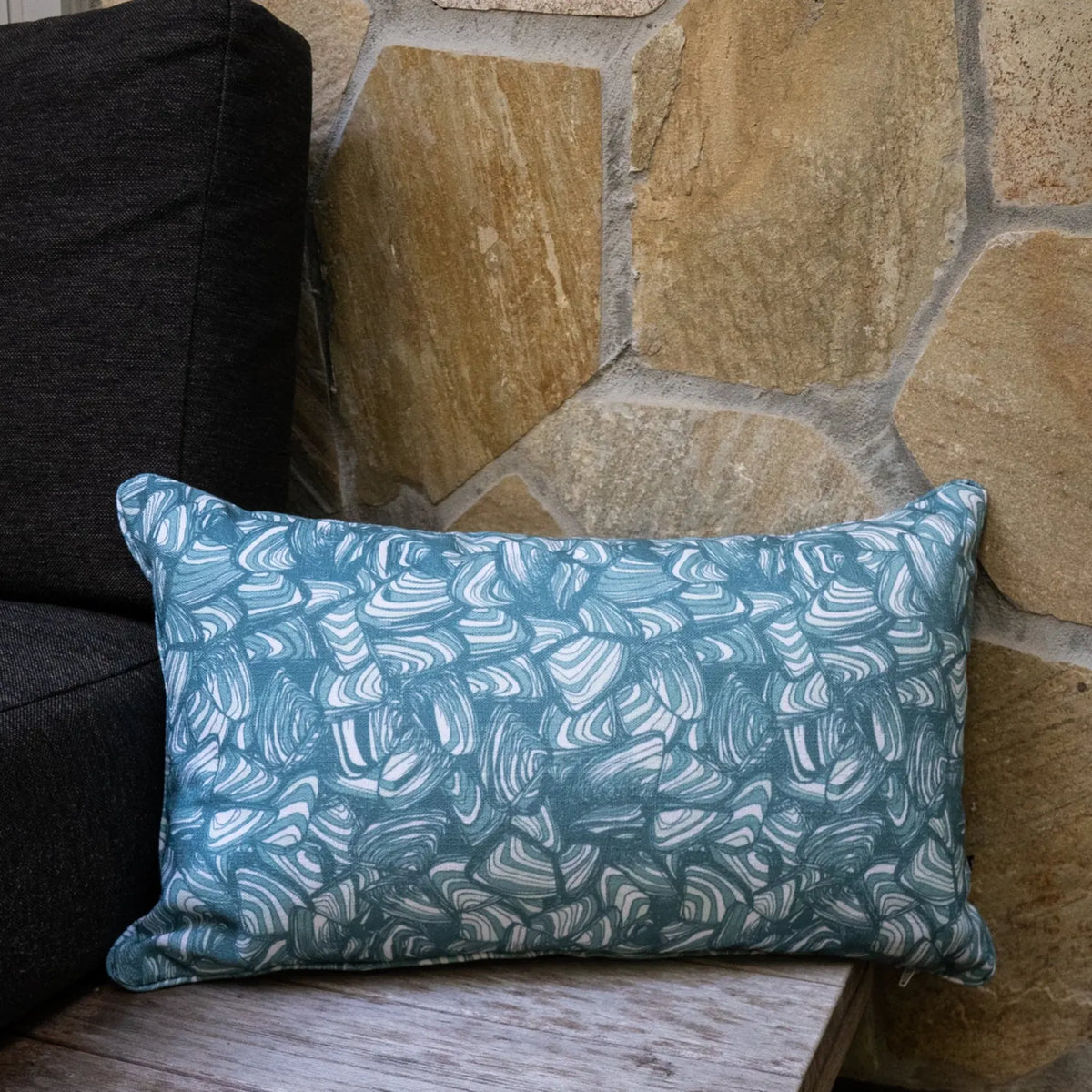 Lumbar outdoor and indoor cushion in the Frenchmans colourway featuring the Pipi pattern, styled on a timber chair beside a stone wall.
