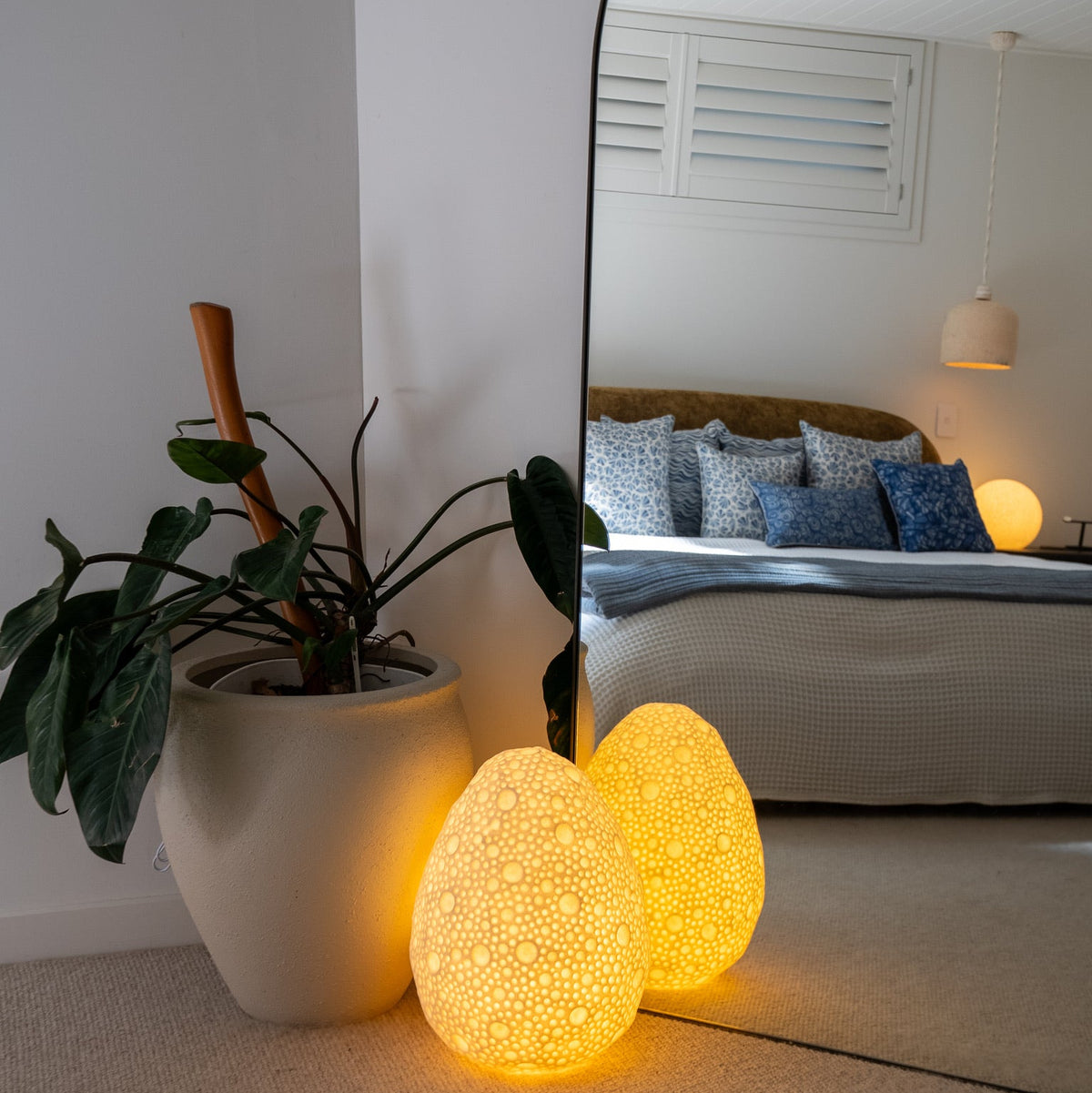 Dotted Oval Reef Lamp glowing warmly beside a bedroom mirror and indoor plant