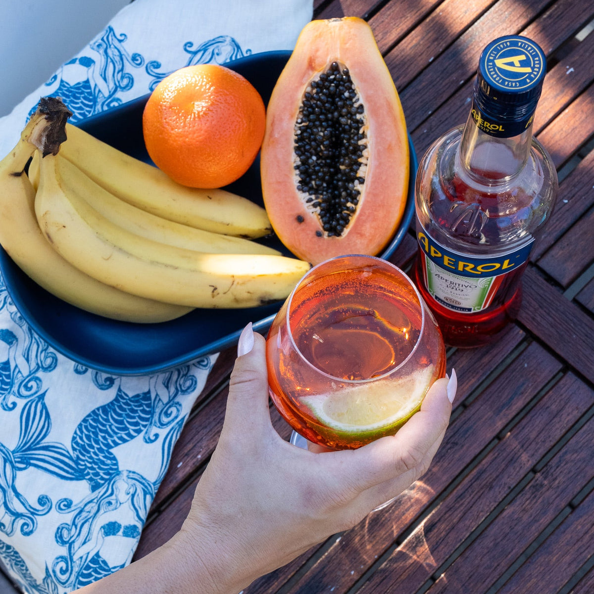 Mermaids Blue linen tea towel styled beside fresh fruit and an Aperol drink on an outdoor table