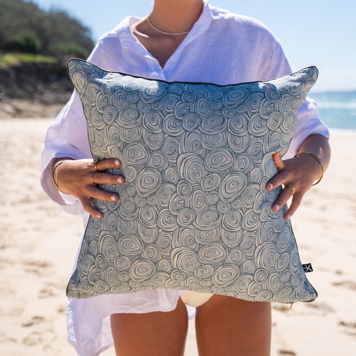 Frenchmans Growth Rings linen cushion cover in blue and natural tones held on the beach