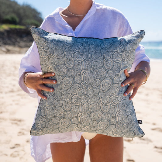Frenchmans Growth Rings linen cushion cover in blue and natural tones held on the beach