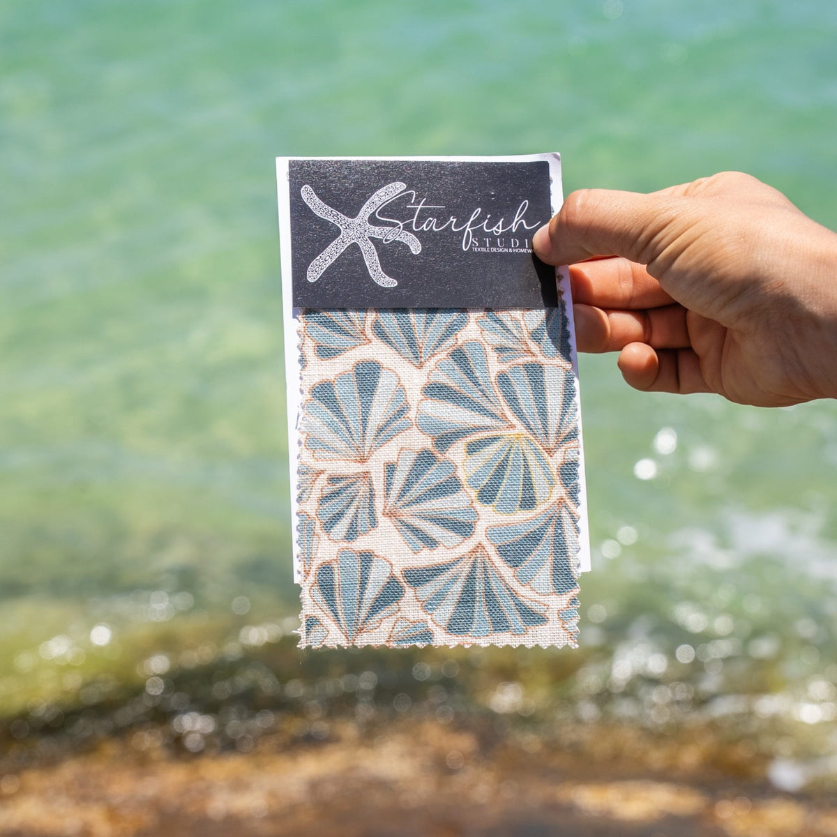 Hand holding a fabric swatch card showing the Frenchmans Shells pattern by Starfish Studio.