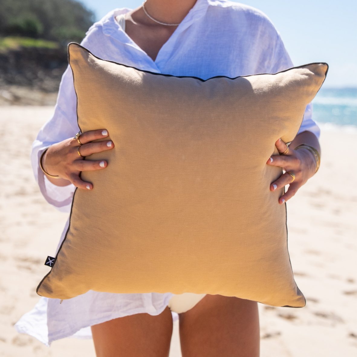 Back view of the Frenchmans Shells linen cushion cover showing the plain natural linen reverse on the beach.