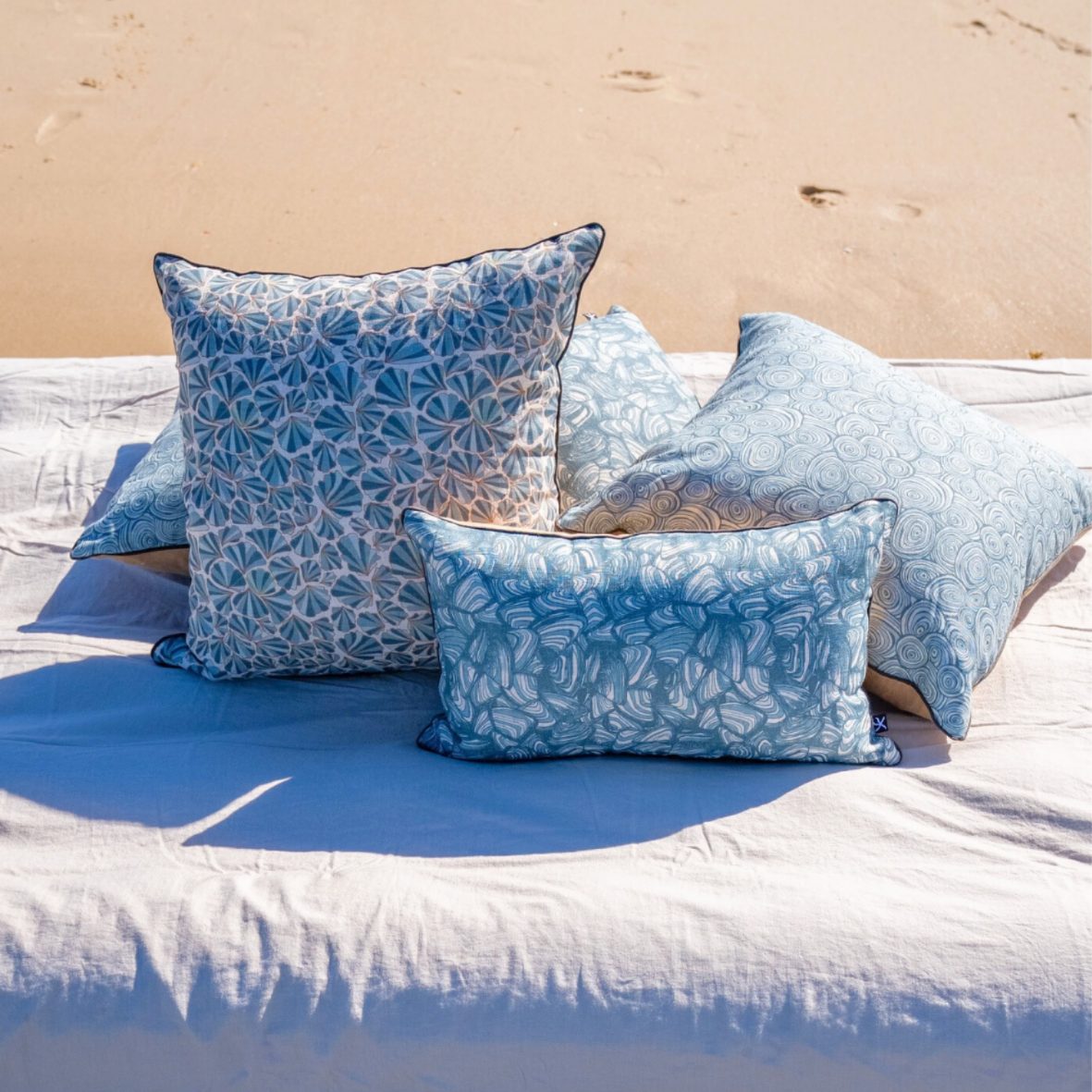 Frenchmans Shells linen cushion cover styled on a beach setting with coordinating Starfish Studio cushions.