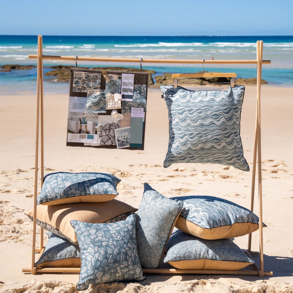 Frenchmans collection linen cushion covers displayed on a wooden stand on the beach, including the Frenchmans Shells design.