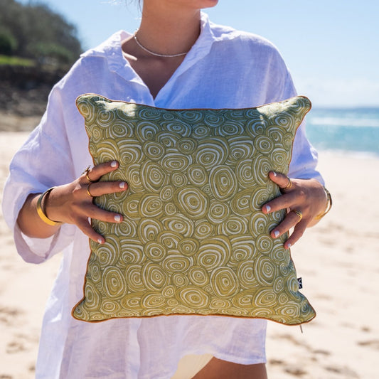 Growth Rings linen cushion cover with green circular print and ochre piping held on the beach