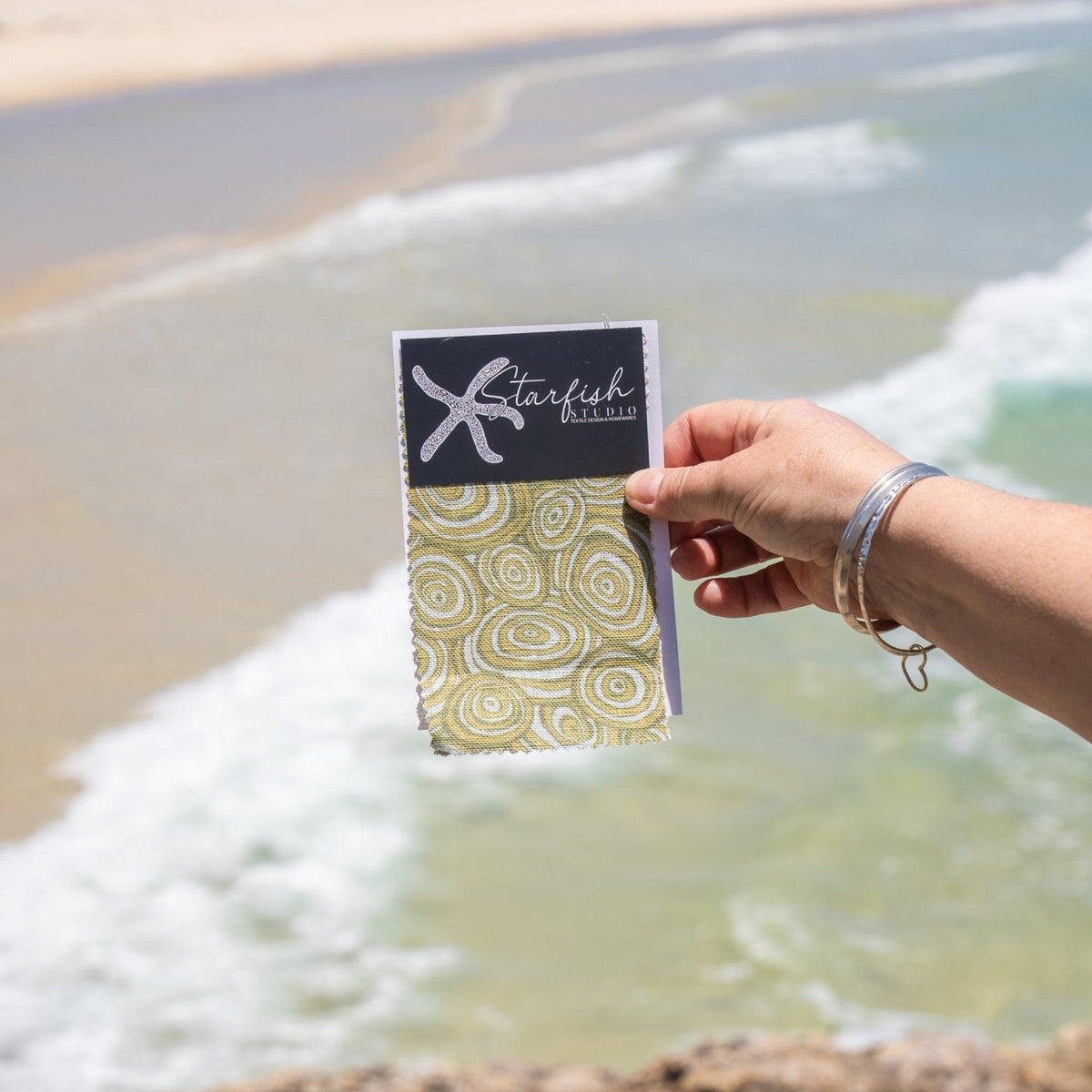 Growth Rings green linen fabric swatch from Starfish Studio held beside the beach