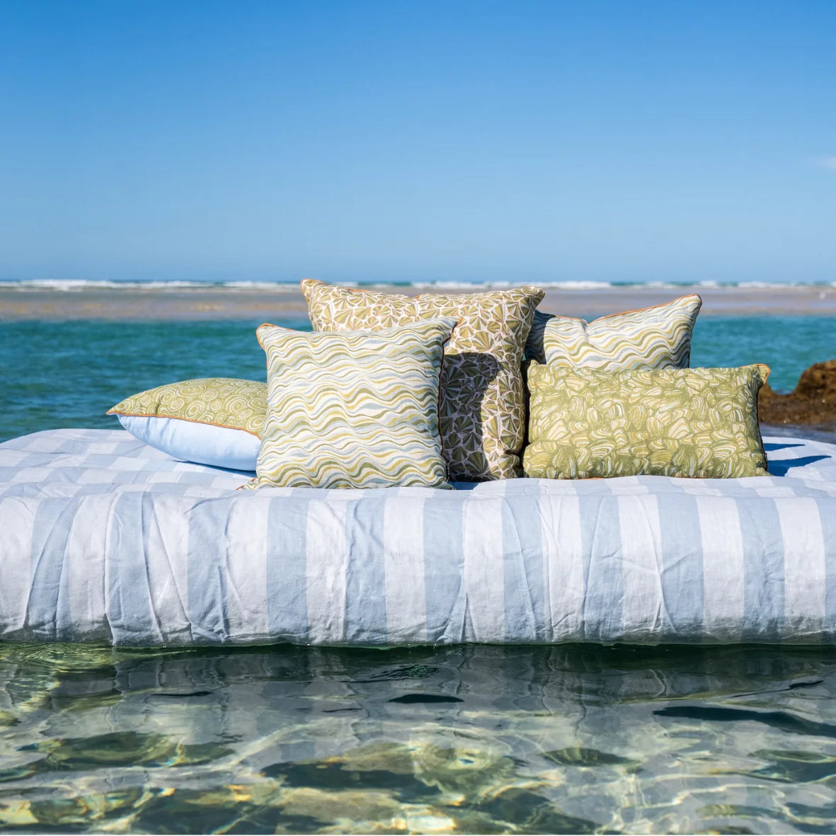 Starfish Studio coastal linen cushion collection styled over clear water, featuring Shells with coordinating green and blue designs.