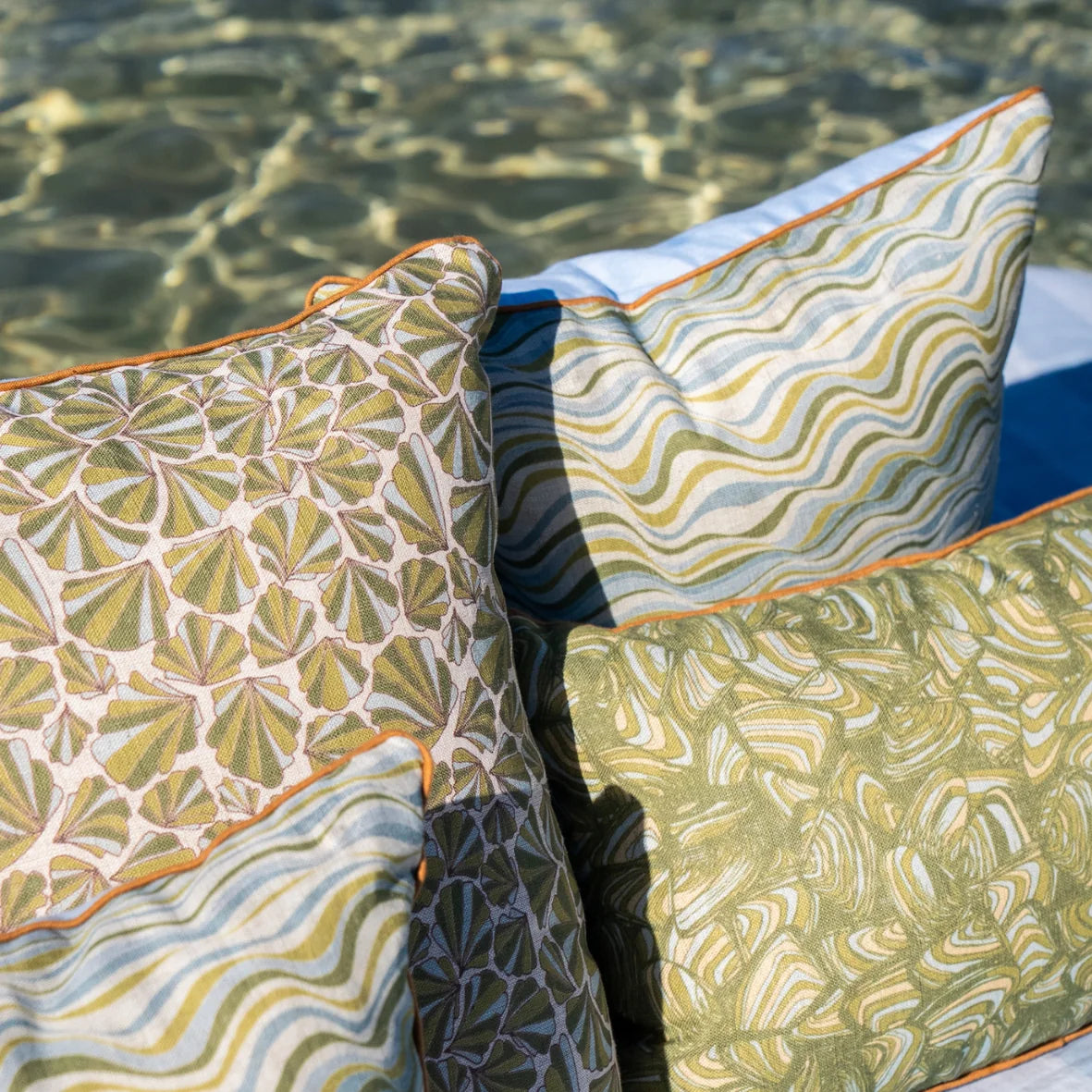 Close-up of Shells linen cushion cover styled with coordinating Straddie Stripe and Pipi designs in green and blue coastal tones.