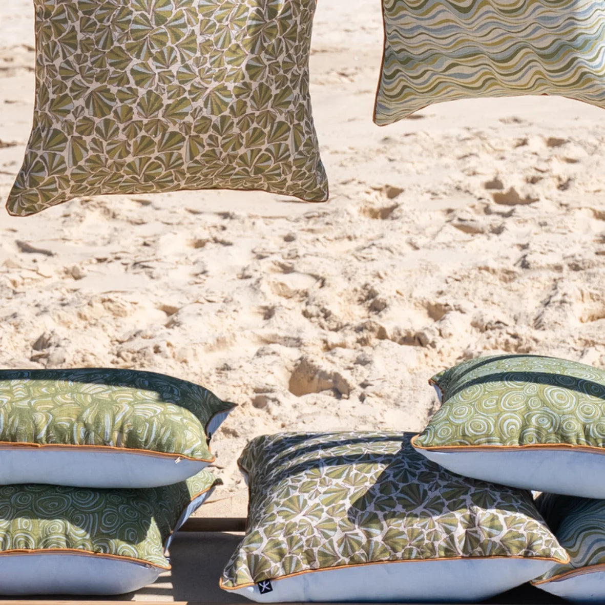 Starfish Studio coastal linen cushion collection stacked on the beach, including Shells, Growth Rings, Pipi and Straddie Stripe designs.