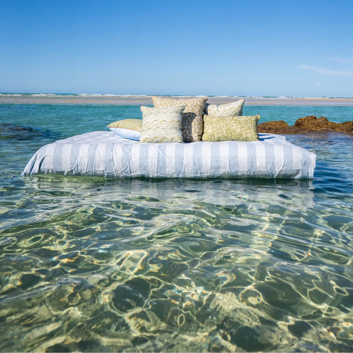 Starfish Studio coastal linen cushion collection styled over clear water, including the olive green Pipi cushion design.