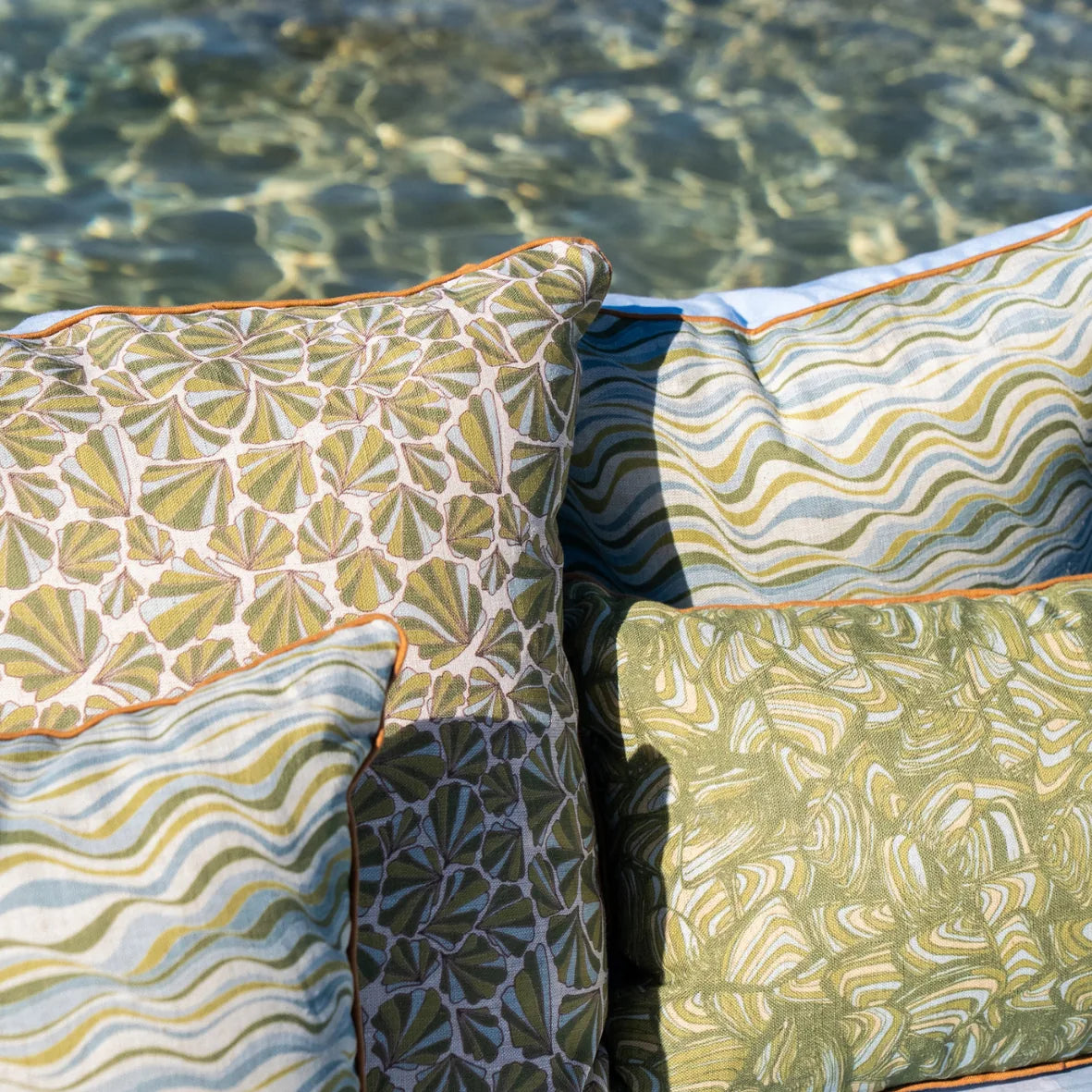 Close-up of Starfish Studio linen cushion covers styled together, including Pipi, Shells and Straddie Stripe designs in green and blue tones.