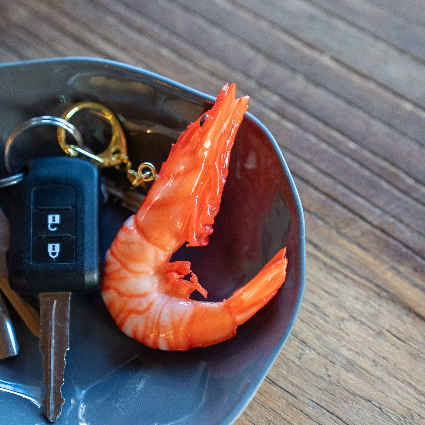 Keychain with a key and a cooked shrimp in a blue bowl on a wooden surface