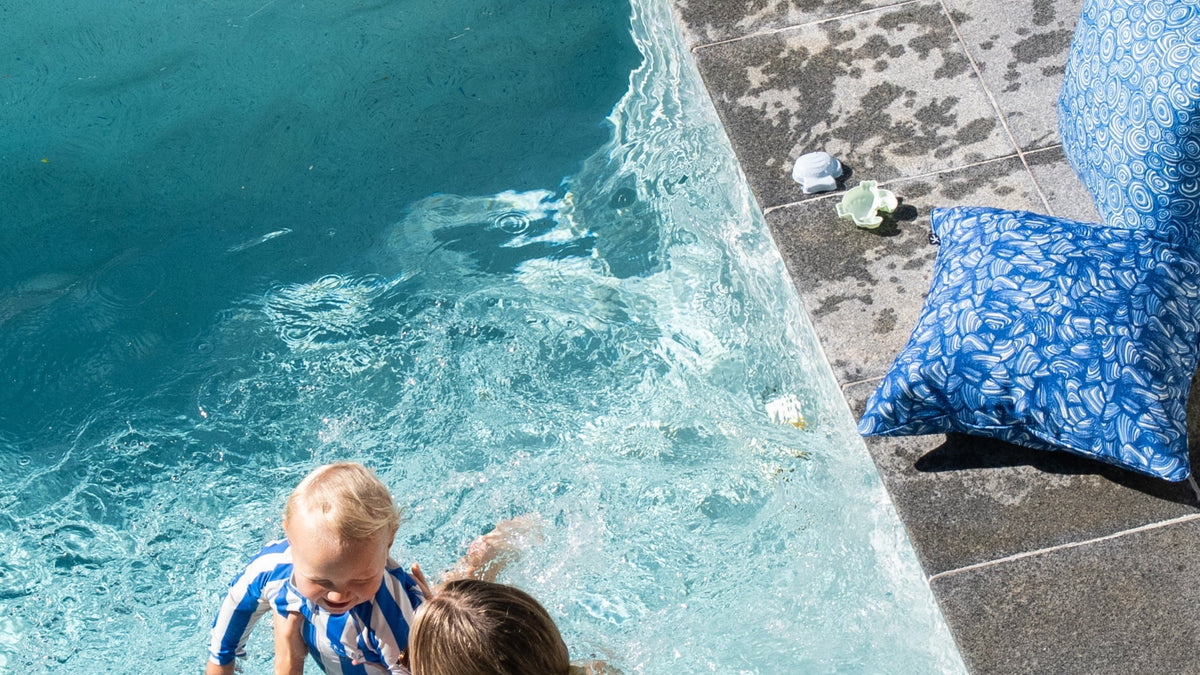 Pacific outdoor cushions styled beside a swimming pool with an adult and child in the water.