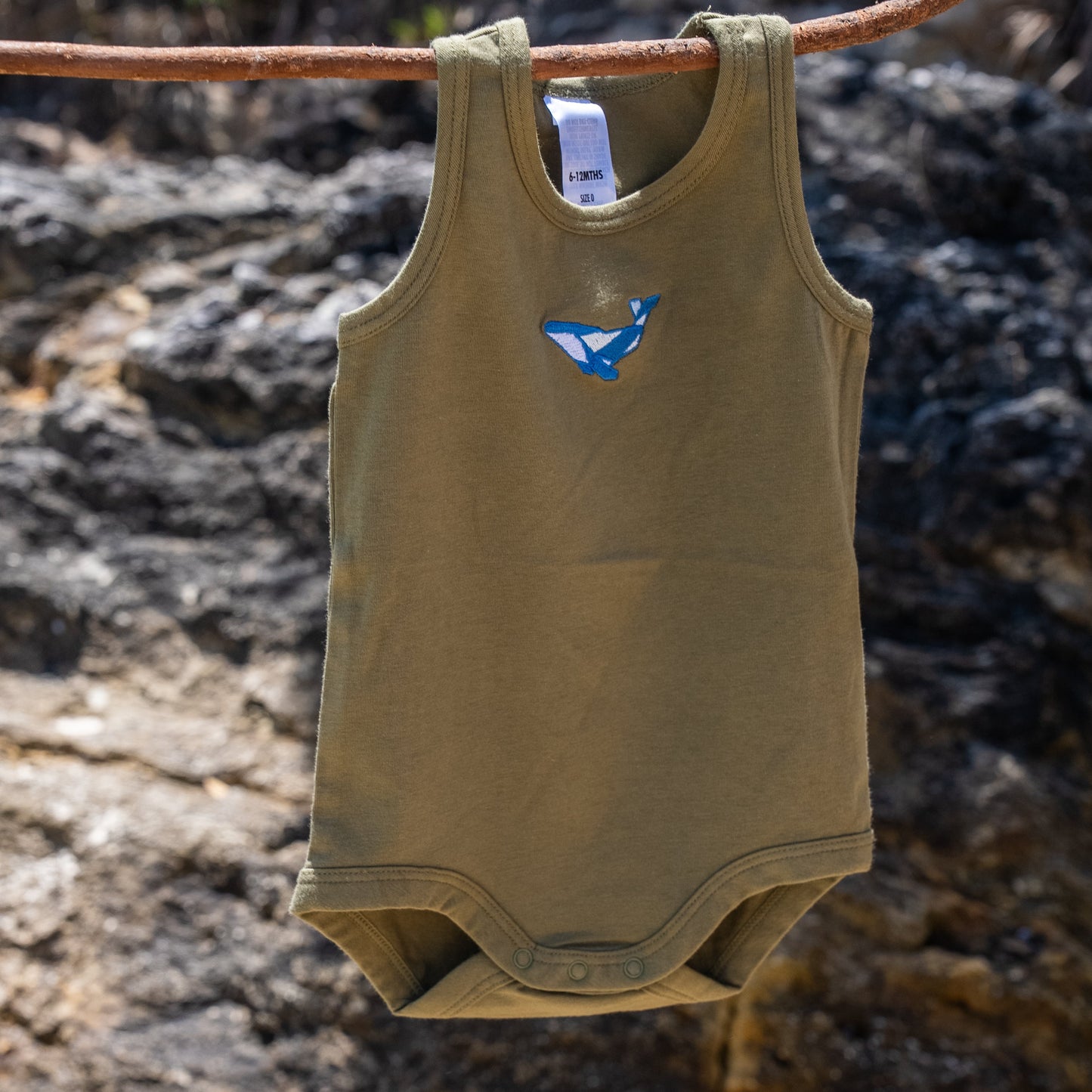 Green baby romper with a blue whale design hanging on a branch against a natural background.