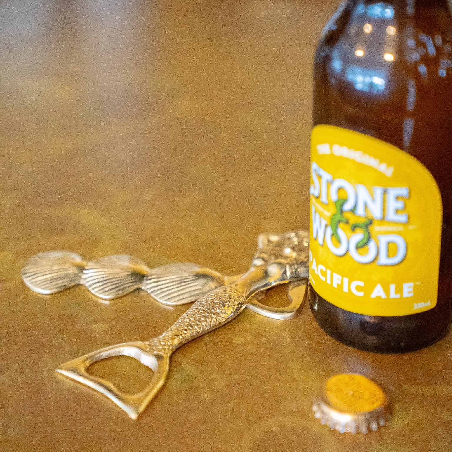 Brown beer bottle with yellow label and gold bottle opener on a reflective surface