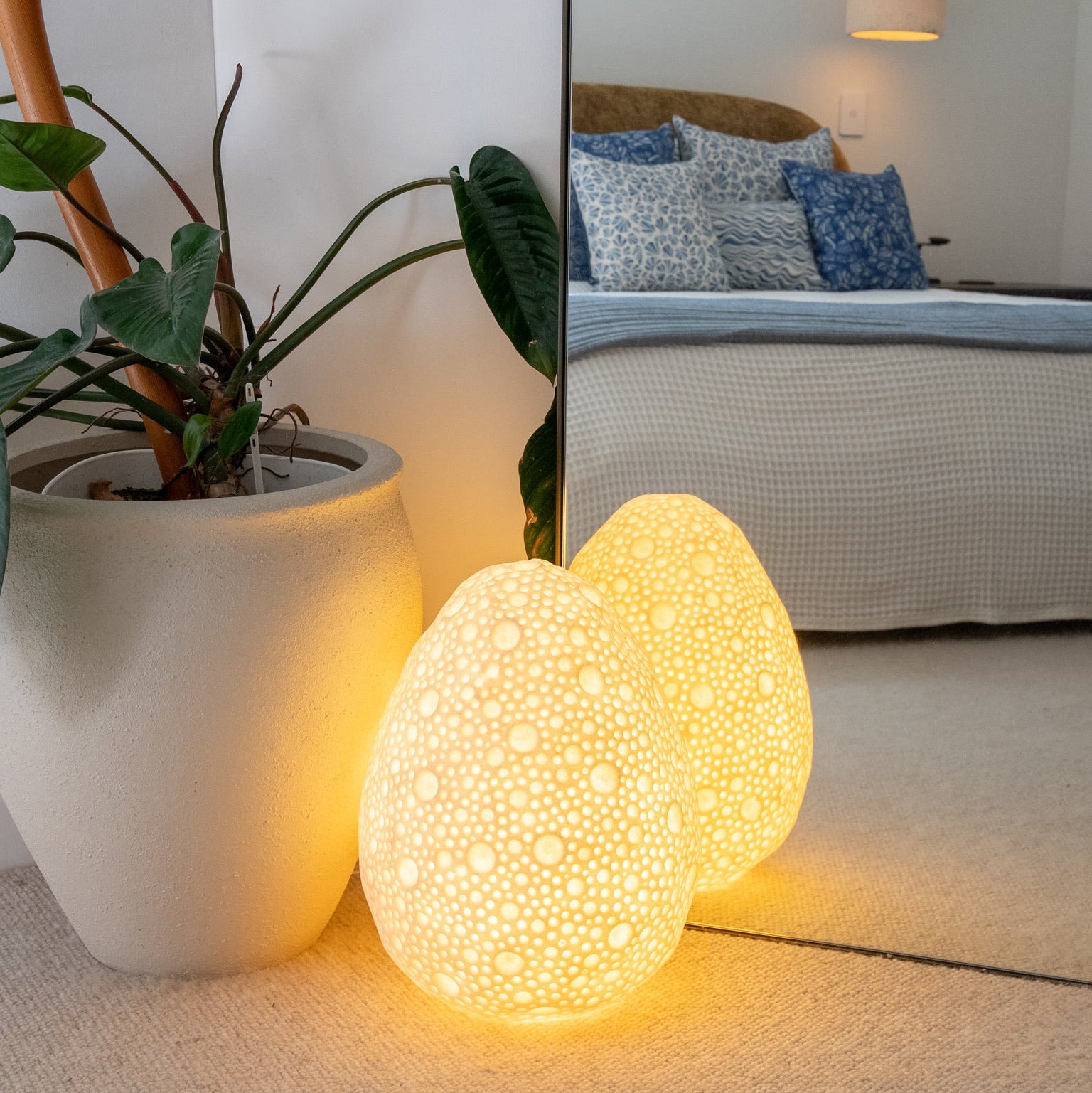 Egg-shaped night light on a carpeted floor with a plant and mirror reflecting a bedroom in the background.