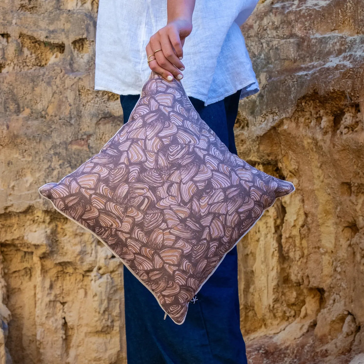 Claytons Pipi linen cushion cover held outdoors in front of sandstone cliffs
