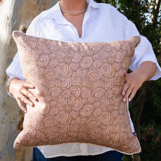 Woman holding square Claytons Growth Rings linen cushion cover in warm brown and natural tones