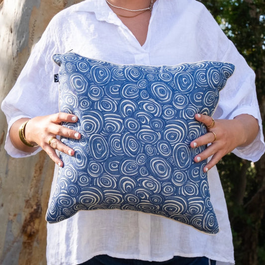 Woman holding square Pacific Growth Rings linen cushion cover in blue and natural tones