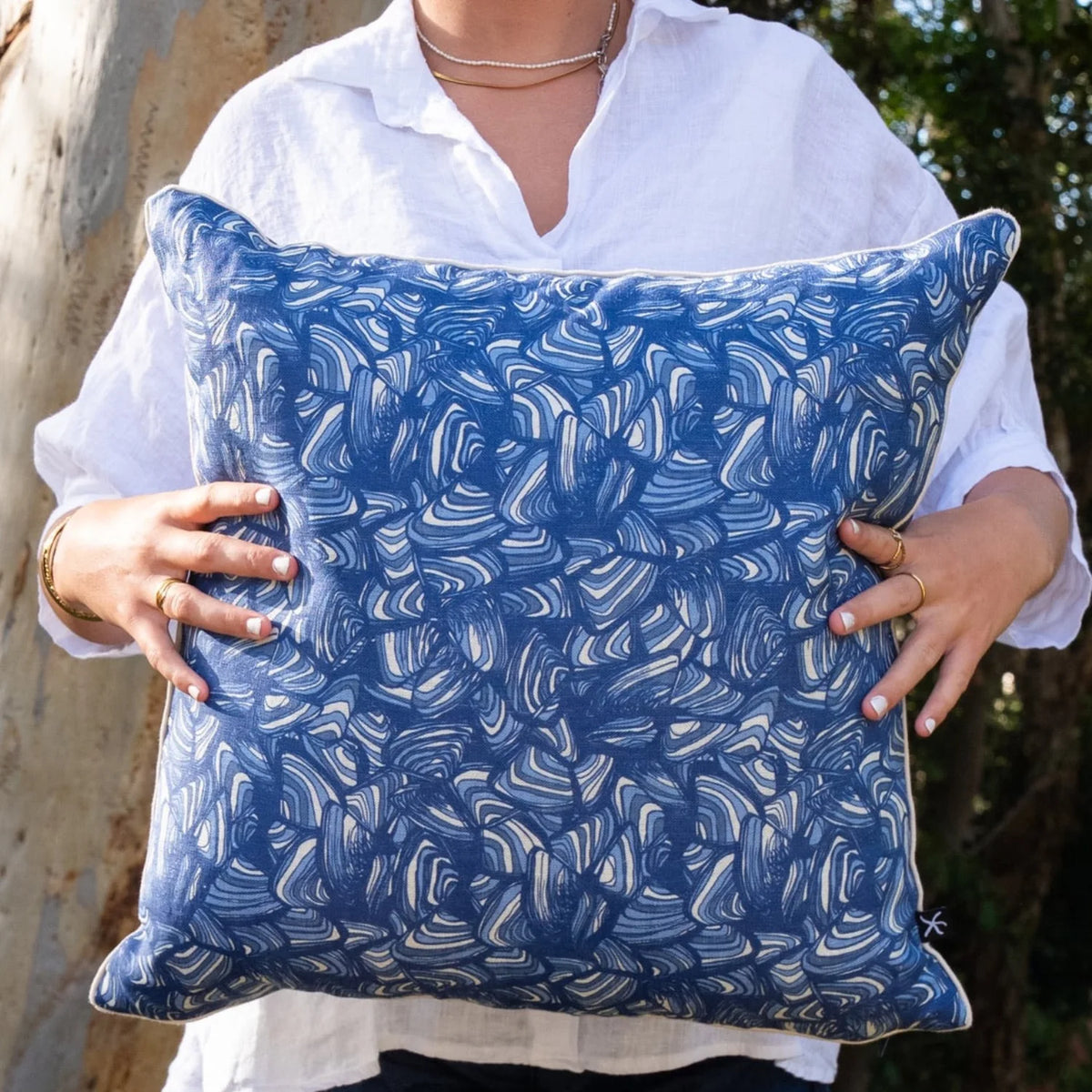 Woman holding square Pacific Pipi linen cushion cover in blue and natural tones