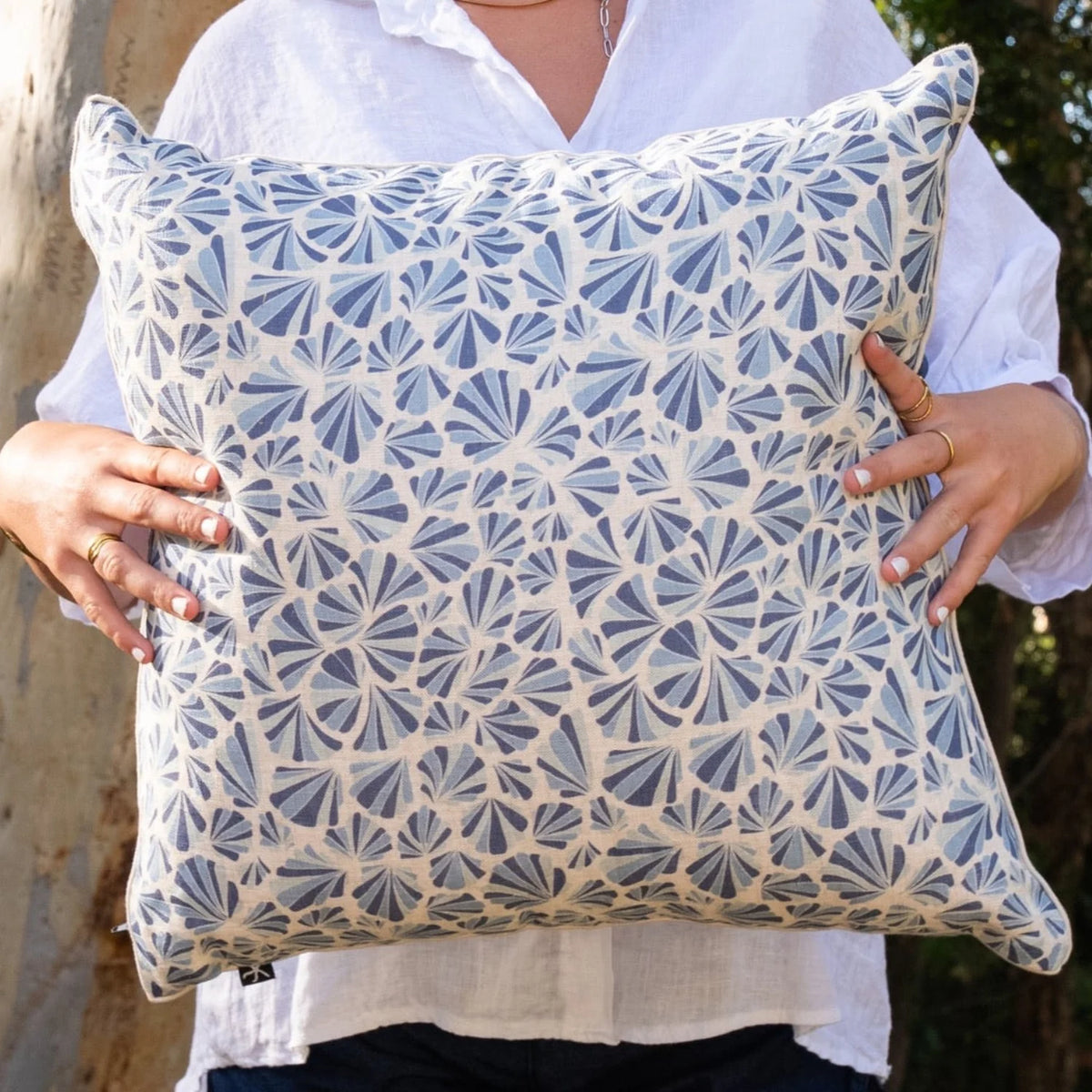 Woman holding square Pacific Shells linen cushion cover in blue and natural coastal tones