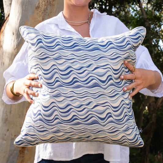 Woman holding square Pacific Straddie Stripe linen cushion cover in soft blue and navy tones