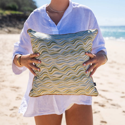 Woman holding Straddie Stripe linen cushion cover in green and blue coastal tones at the beach