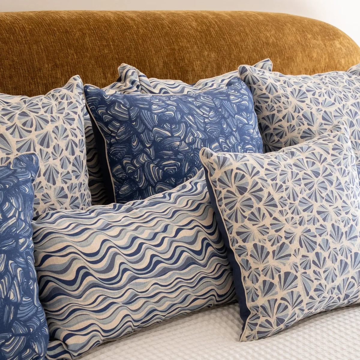 Pacific Shells linen cushion covers styled with coordinating blue coastal cushions on a bed