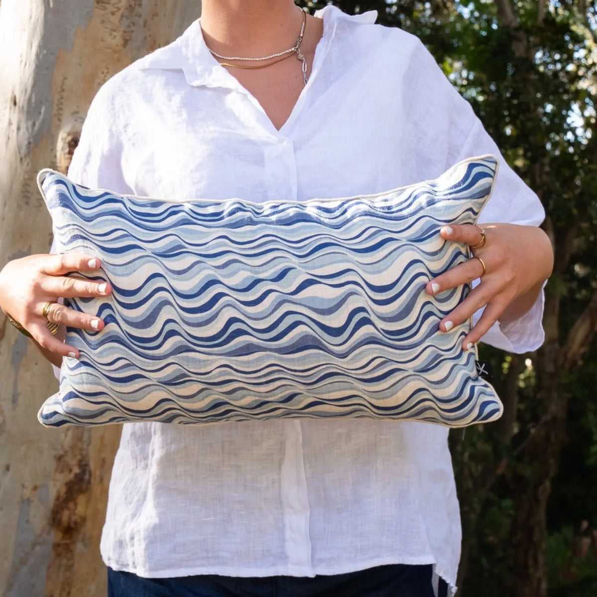 Woman holding rectangular Pacific Straddie Stripe linen cushion cover in blue coastal tones