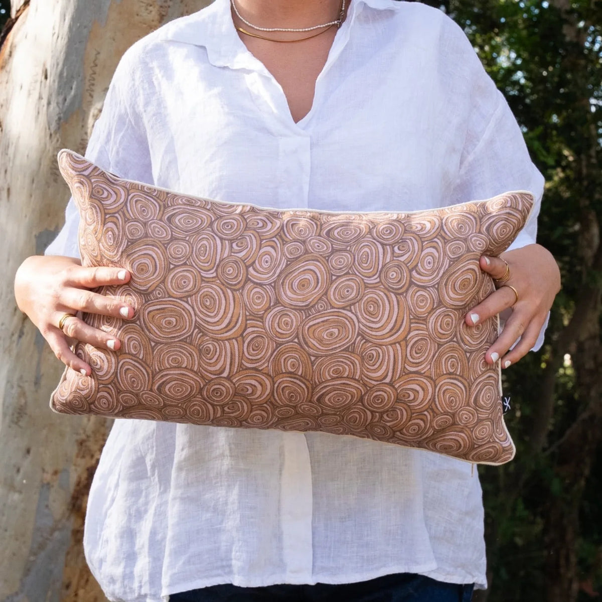Woman holding rectangular Claytons Growth Rings linen cushion cover in earthy brown tones