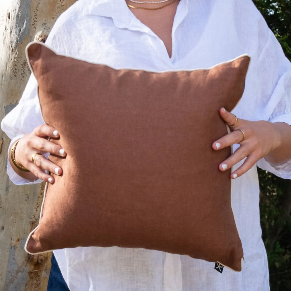 Woman holding the warm brown linen reverse of a square Claytons Straddie Stripe cushion cover