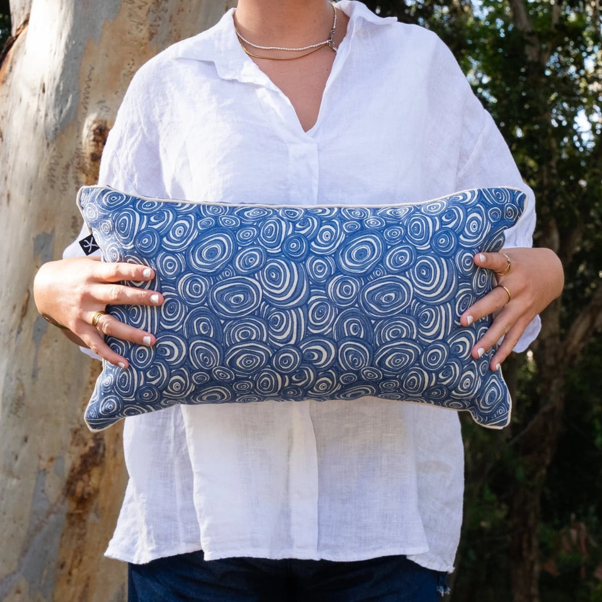 Woman holding rectangular Pacific Growth Rings linen cushion cover in blue and natural tones