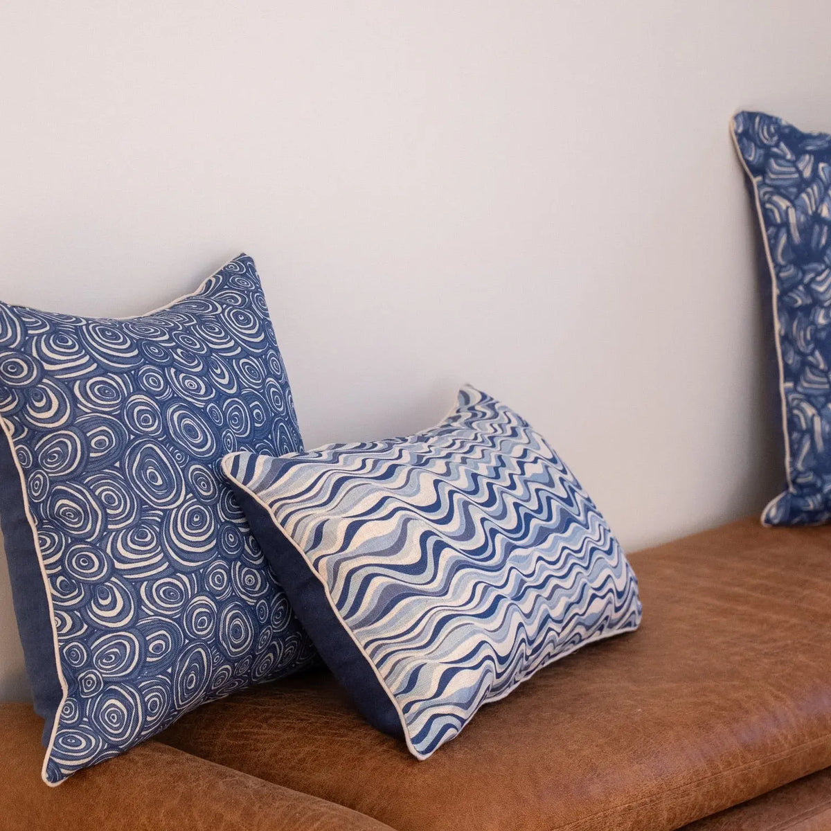 Pacific Straddie Stripe linen cushion cover styled with coordinating blue coastal cushions on a leather lounge