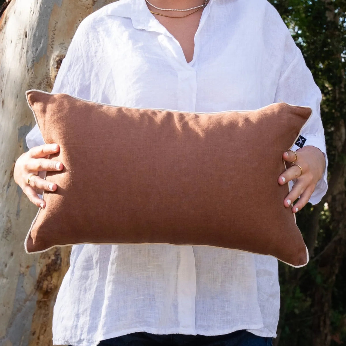 Woman holding warm brown linen reverse of Claytons Growth Rings rectangular cushion cover