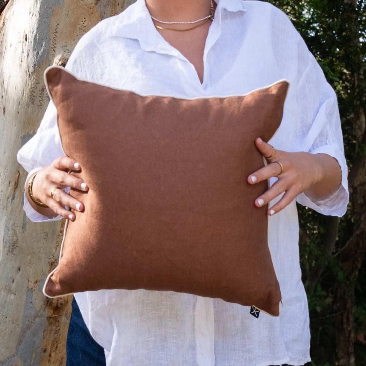 Woman holding the warm brown linen reverse of a square Claytons cushion cover
