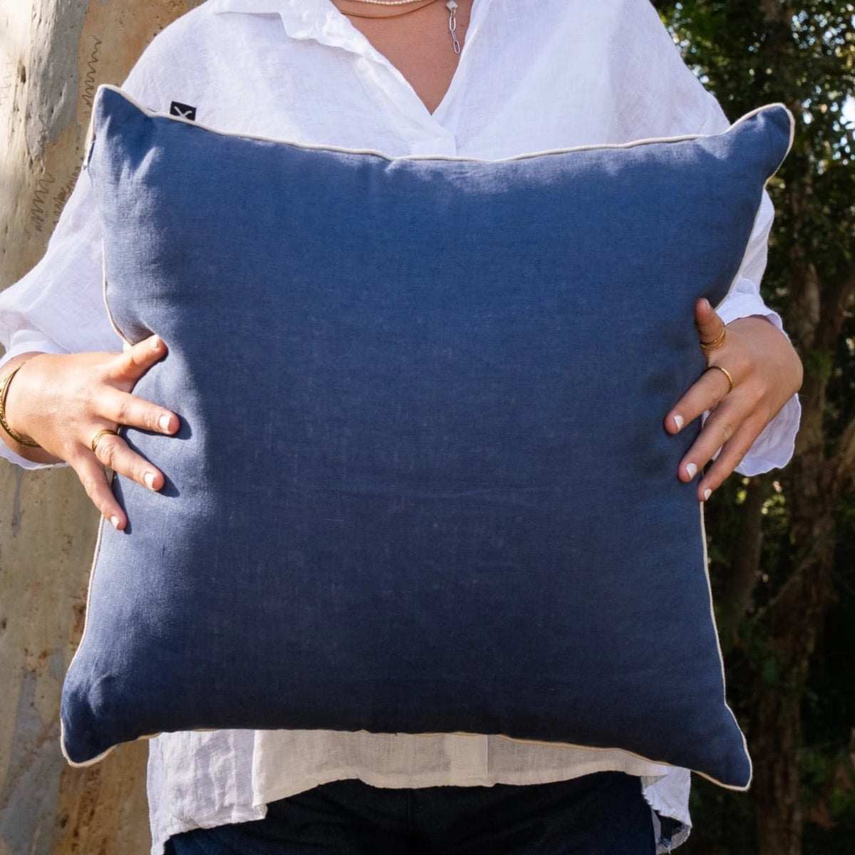 Woman holding navy linen reverse of square Pacific Shells cushion cover with natural piping