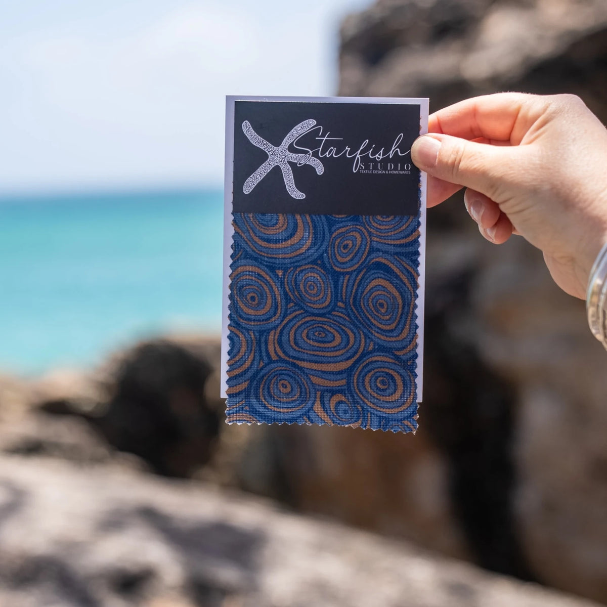 Growth Rings Mariner linen fabric swatch in navy blue and ochre held beside the ocean