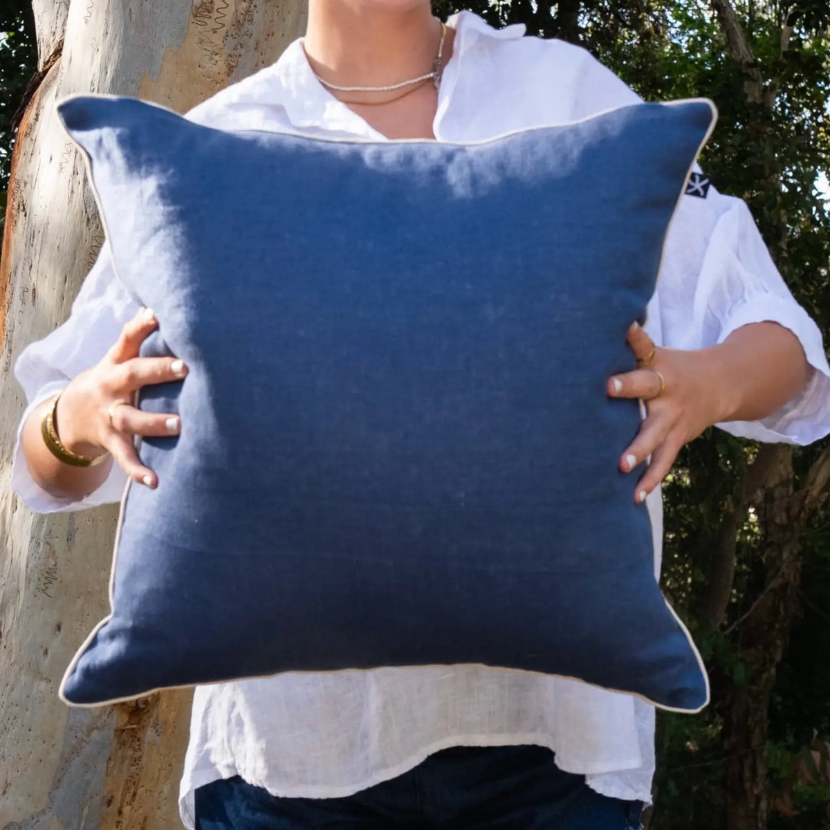 Woman holding navy linen reverse of square Pacific Straddie Stripe cushion cover with natural piping