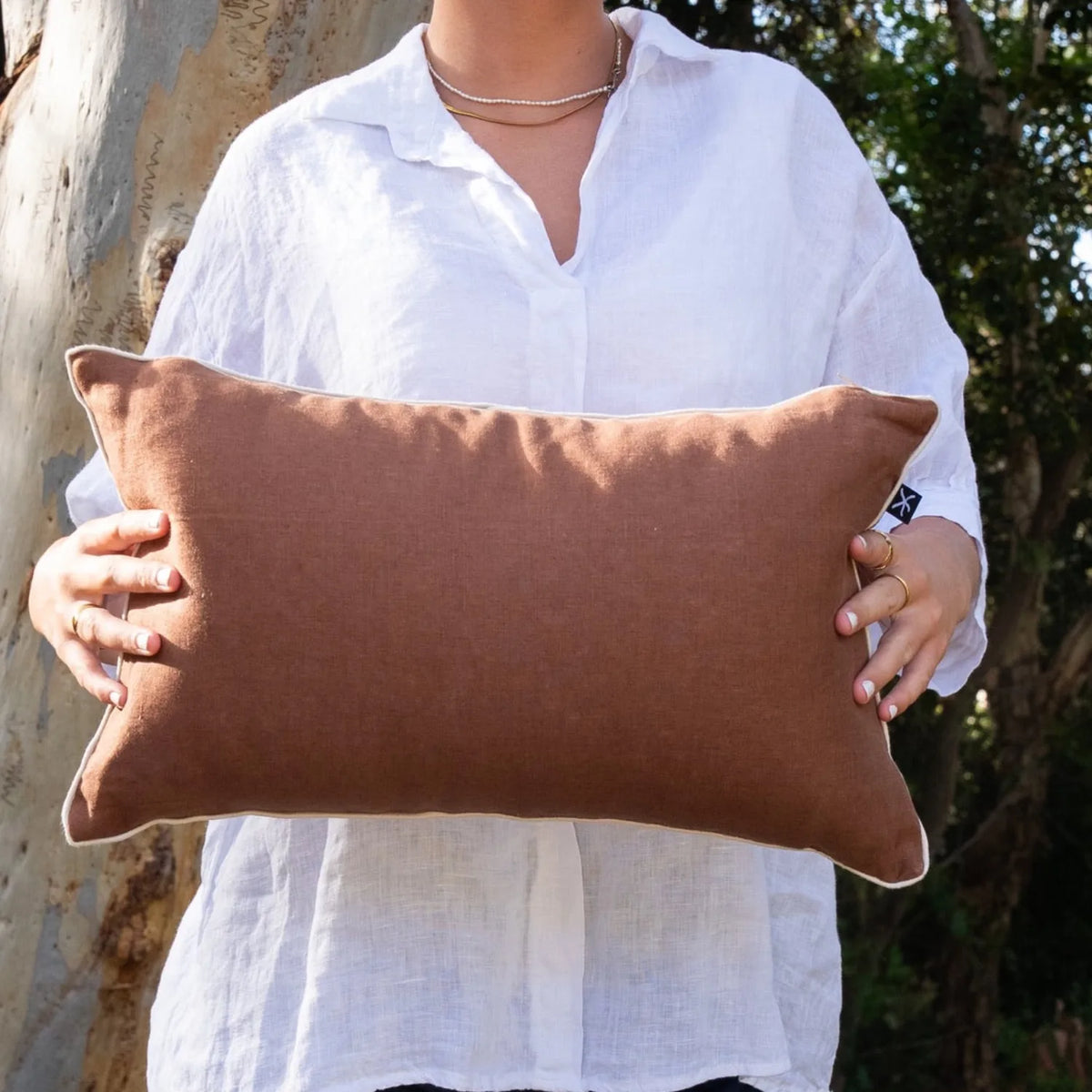 Woman holding the warm brown linen reverse of a rectangular Claytons Straddie Stripe cushion cover