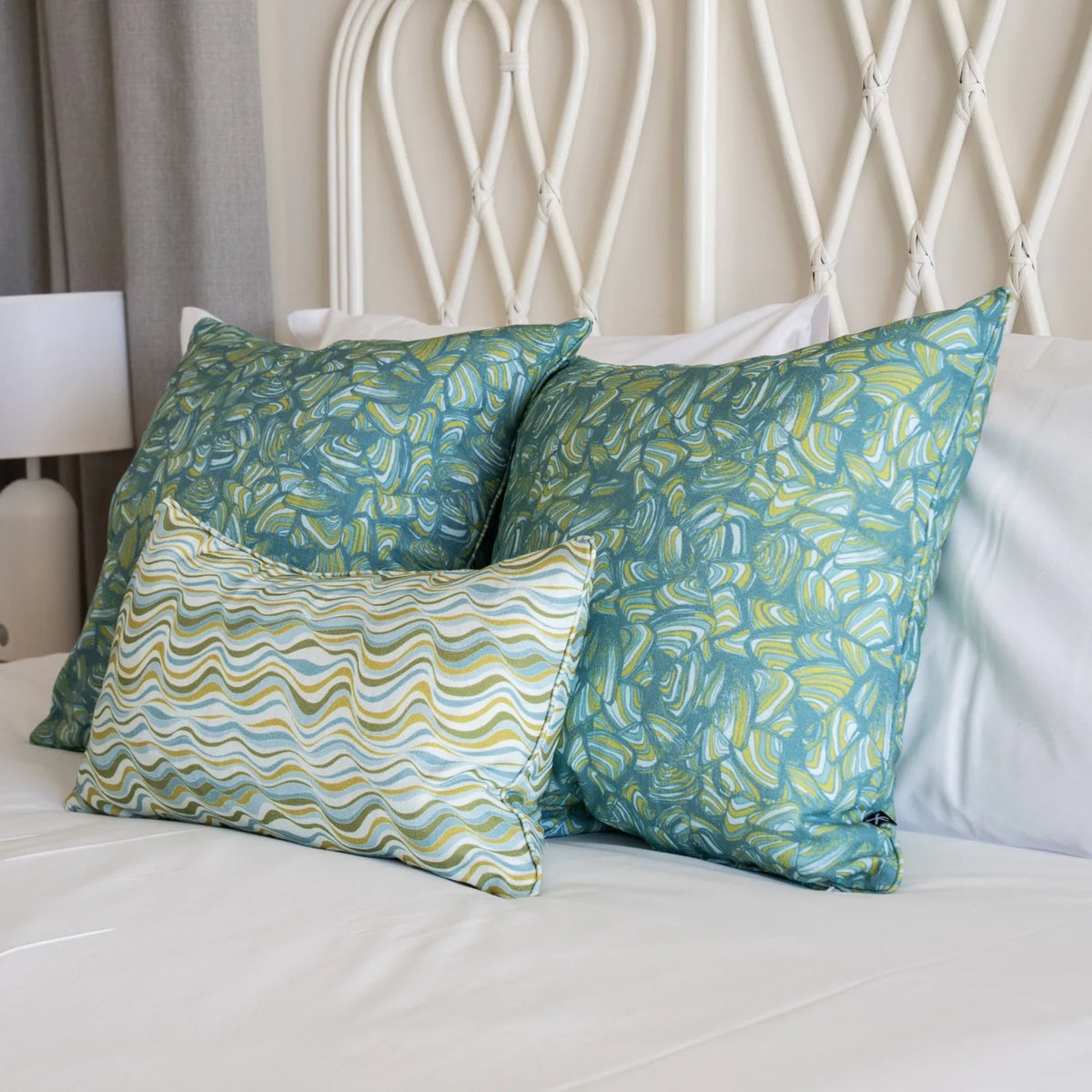 Mangrove cushions styled on a white bed with two Pipi square cushions and a Straddie Stripe lumbar cushion.