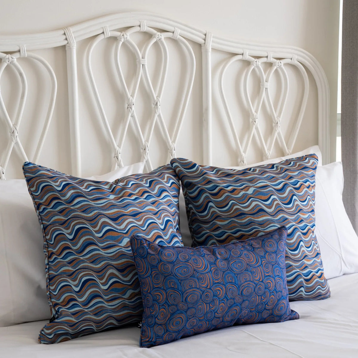Mariner cushions styled on a white bed with two Straddie Stripe pillows and a Growth Rings lumbar cushion.