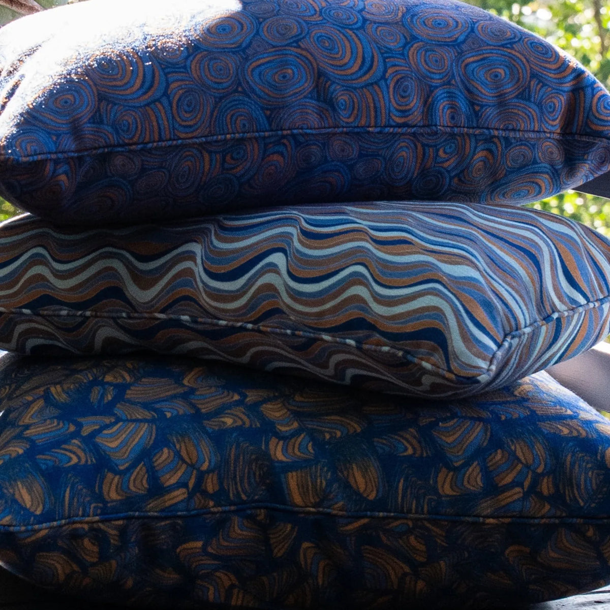 Stacked outdoor cushions including a Mariner colourway Growth Rings cushion with coordinating patterned cushions.