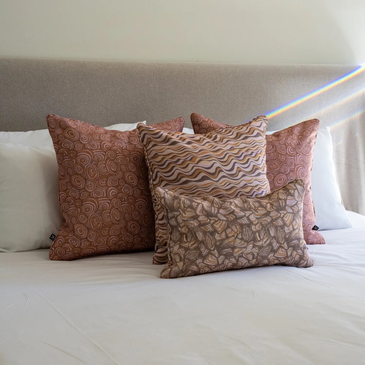 Claytons colourway Growth Rings, Straddie Stripe and Pipi cushions layered together on a white bed.