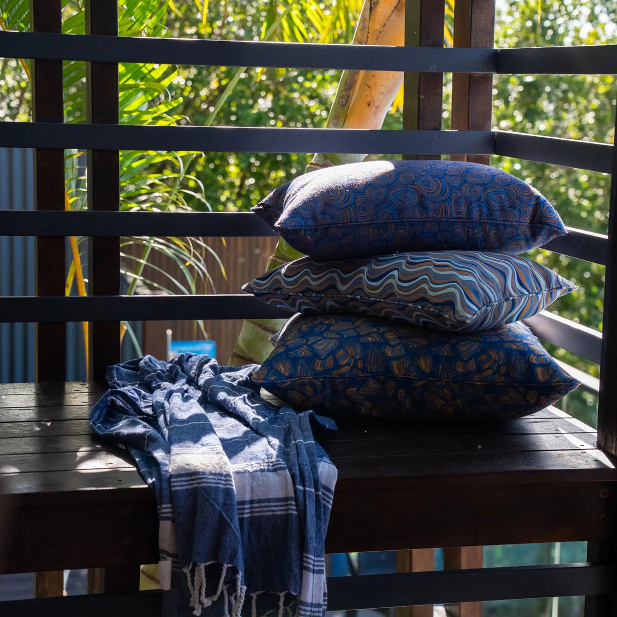 Outdoor styling with stacked cushions, featuring the Mariner colourway Growth Rings pattern with coordinating designs on a timber bench.