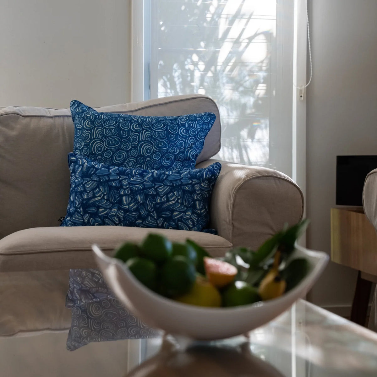 Pacific cushions styled on a beige armchair with a fruit bowl in the foreground.