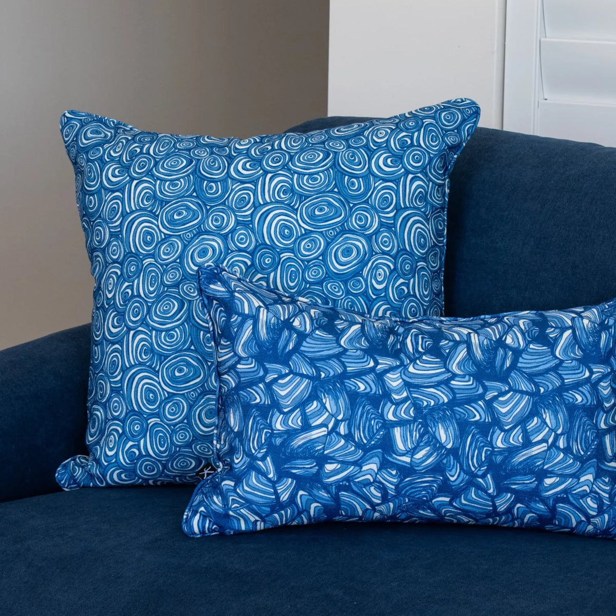 Pacific cushions styled on a blue sofa with a square Growth Rings cushion and a Pipi lumbar cushion.